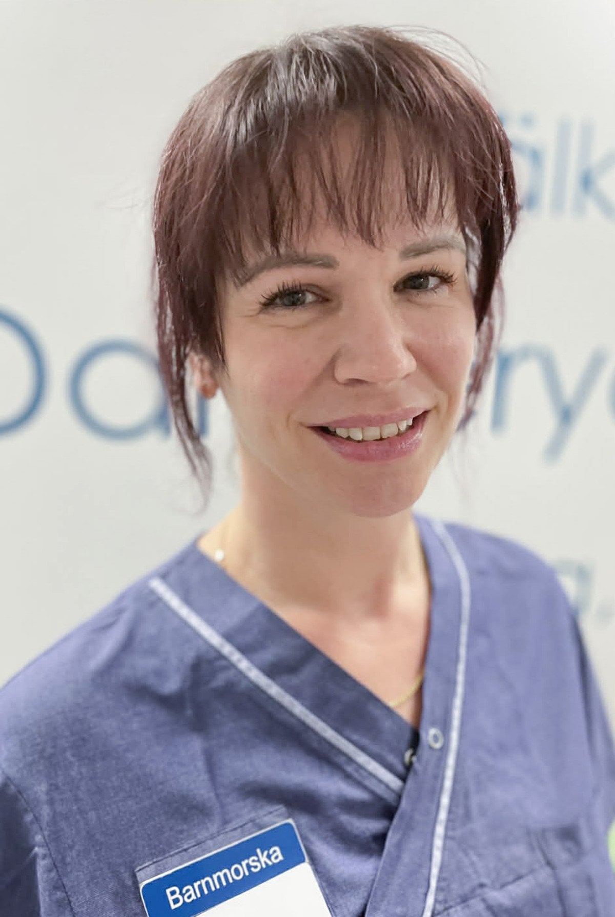 En kvinna i operationskläder ler mot kameran.