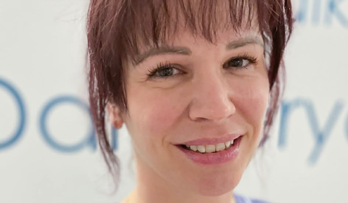 En kvinna i operationskläder ler mot kameran.