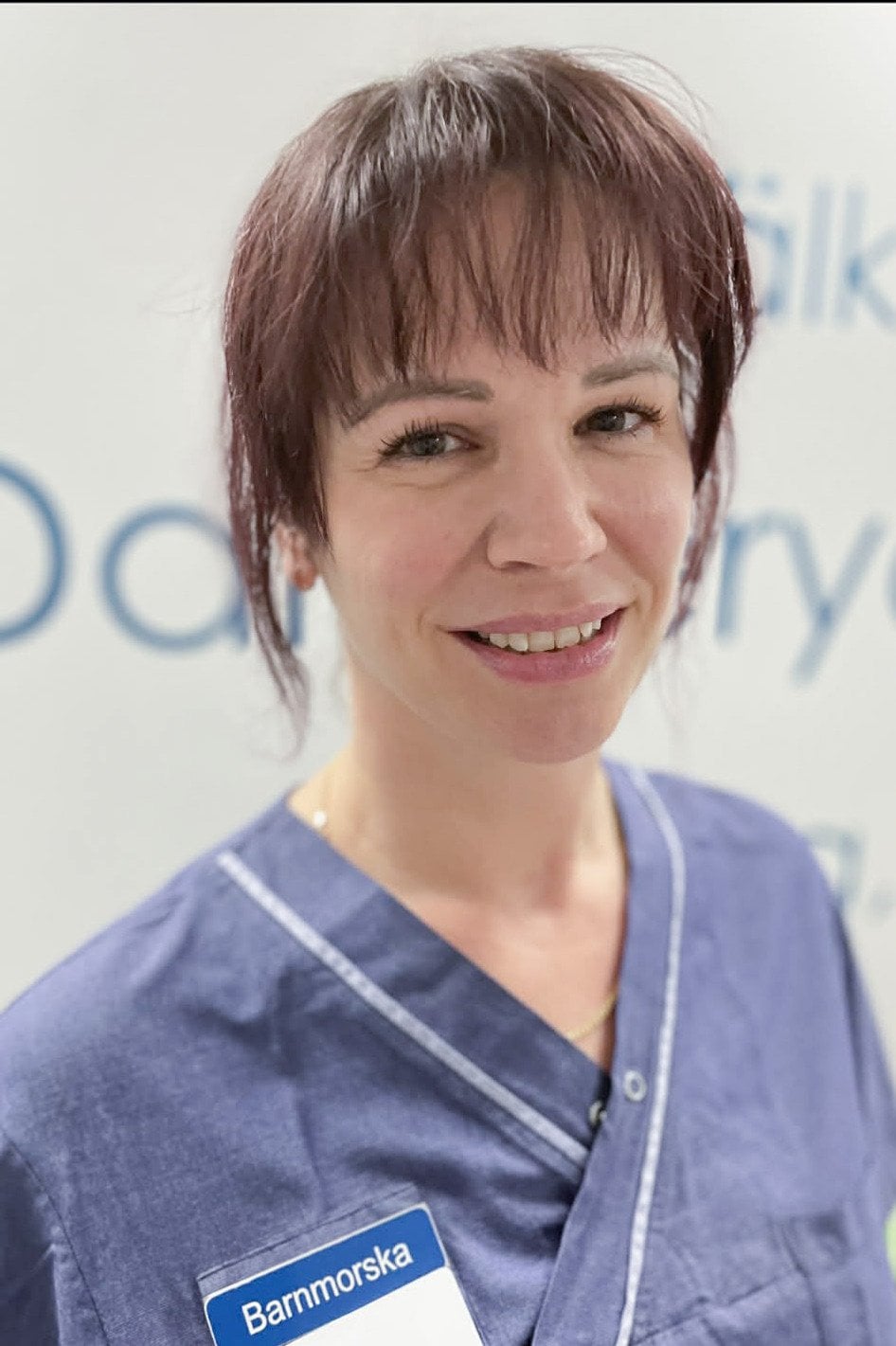 En kvinna i operationskläder ler mot kameran.